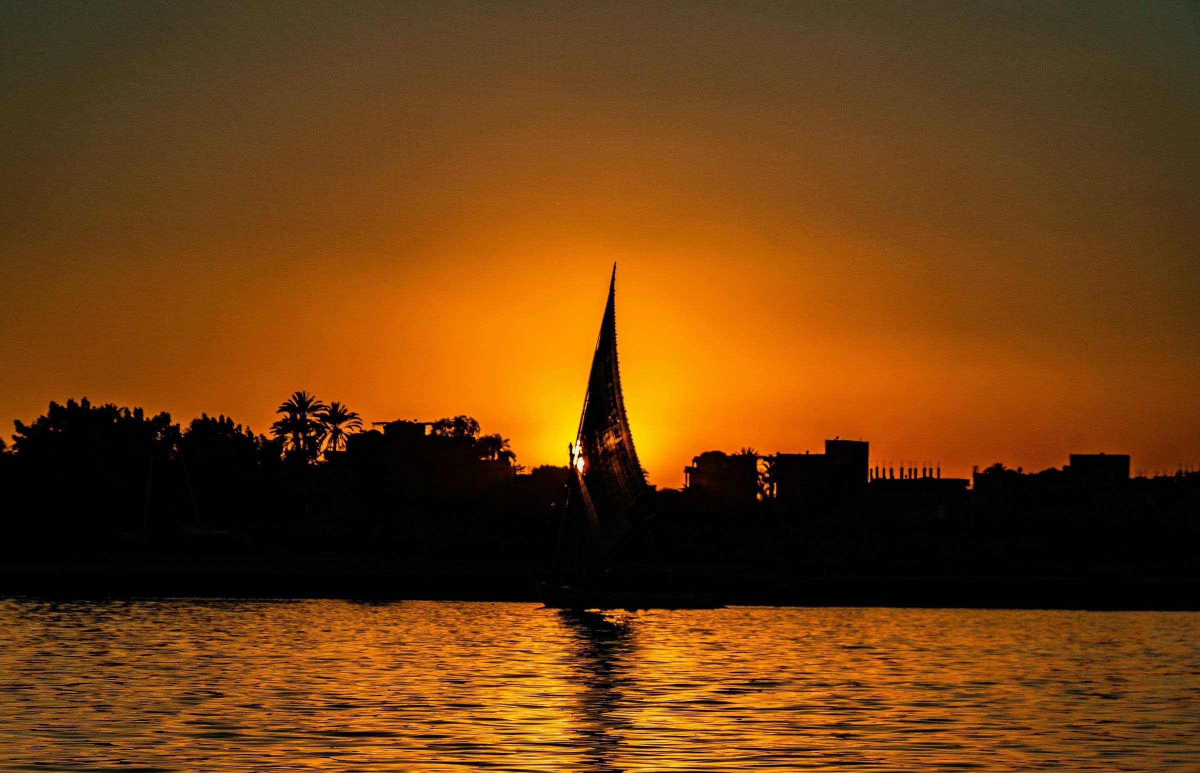 A felucca silhouetted against an orange Nile sunset