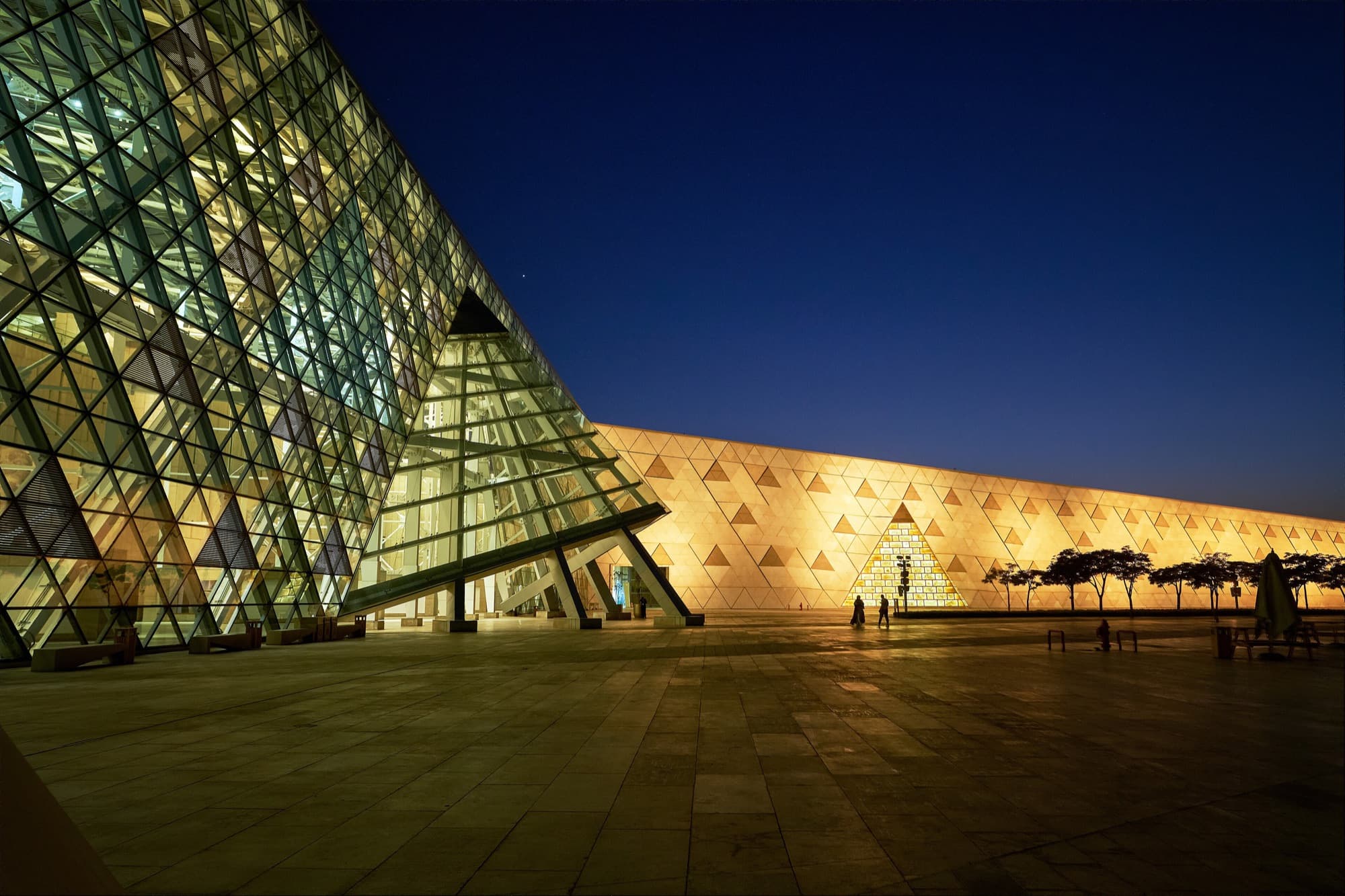 The illuminated glass facade of the Grand Egyptian Museum at night