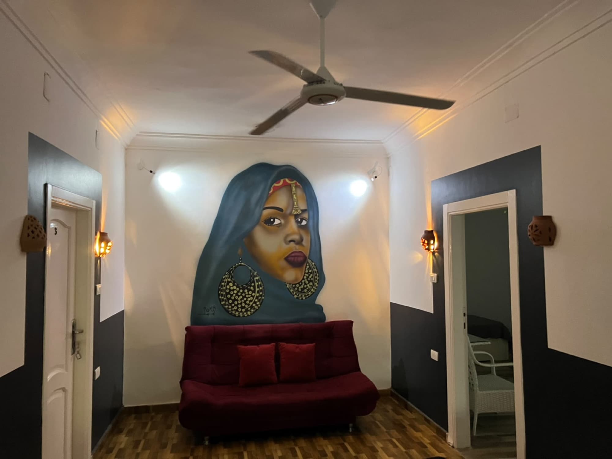 A lounge with a large mural of a Nubian woman above a red sofa