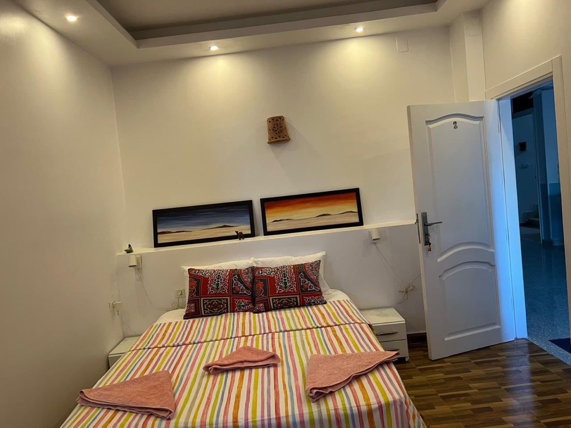 A double room with a striped quilt and paintings of the desert