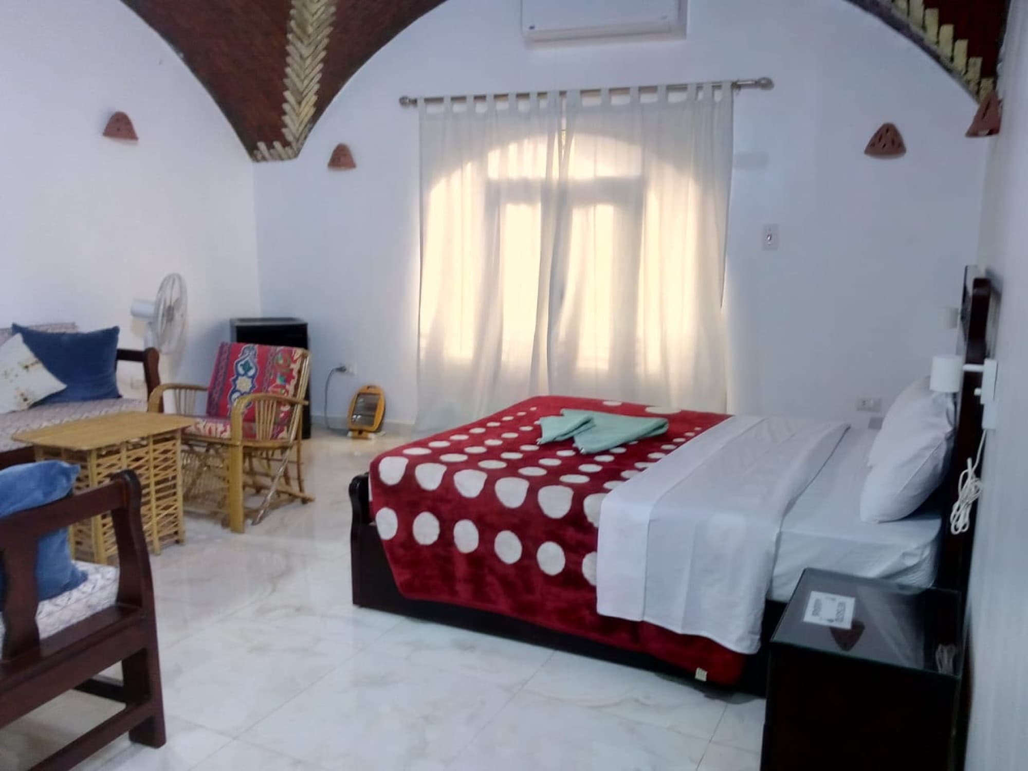 A bright bedroom with a vaulted ceiling, a red quilt and cane chairs