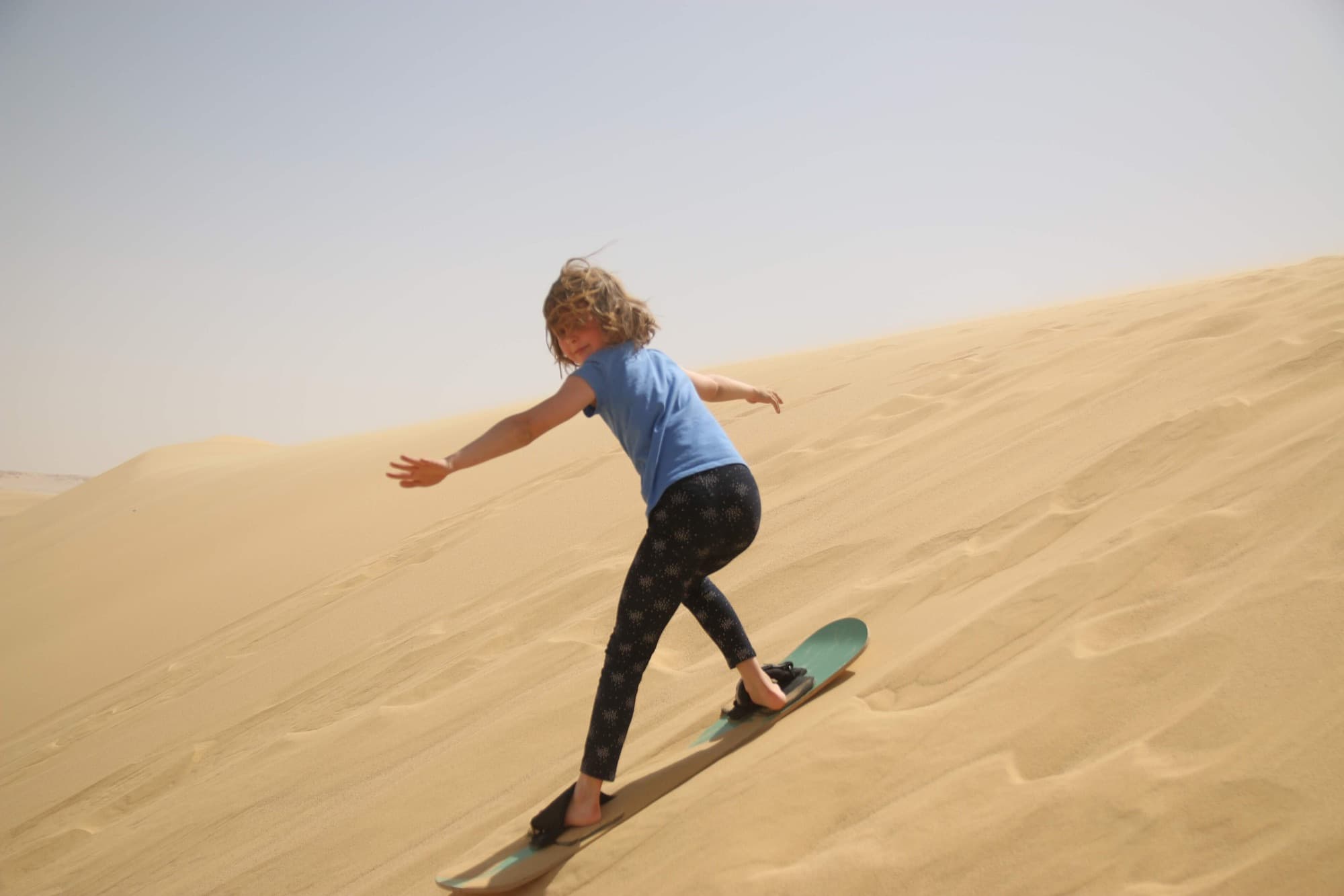 A traveller sandboarding down a steep desert dune in Egypt