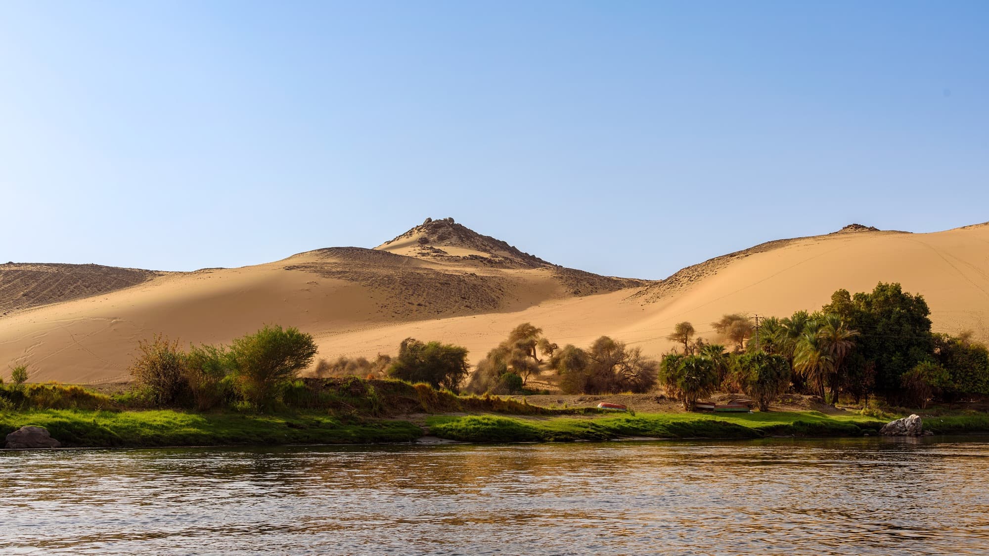 Golden sand dunes rising above palm trees on the banks of the Nile near Aswan